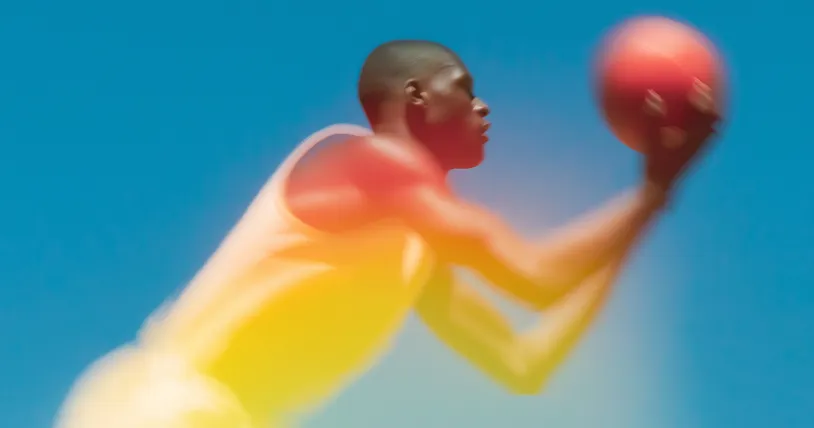 Blurred image of a basketball player in white jersey preparing to shoot a basketball against a clear blue sky.